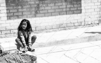 Child Adjusting Sandals by Brick Wall - Child Adjusting Sandals, black and white street photography, Nasrul Eam print, limited edition fine art, childhood photography Nepal
