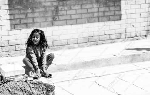Child Adjusting Sandals by Brick Wall