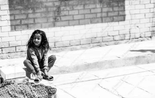 Child Adjusting Sandals by Brick Wall