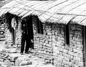 Stone Wall, Thatch Roof, and Peeking Child - Stone Wall Thatch Roof Peeking Child, Nasrul Eam fine art print, Himalayan