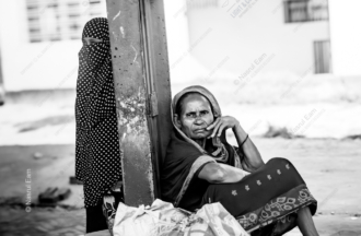 Two Women Waiting by a Post