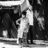 A Woman with a Crutch Beside a Corrugated Wall