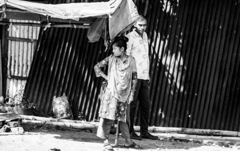 A Woman with a Crutch Beside a Corrugated Wall