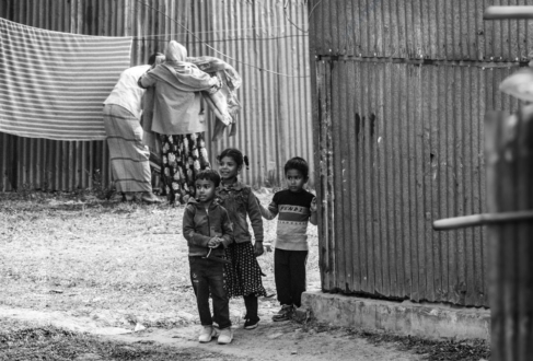 Three Children Standing Beside a Corrugated Metal Wall