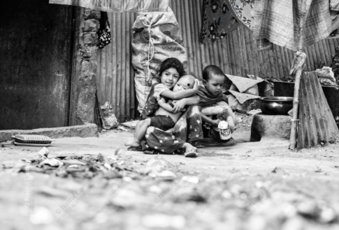 Three Children Seated Against a Corrugated Wall