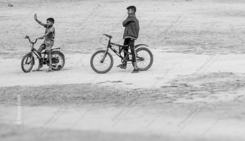 Two Boys on Bicycles Across an Open Field